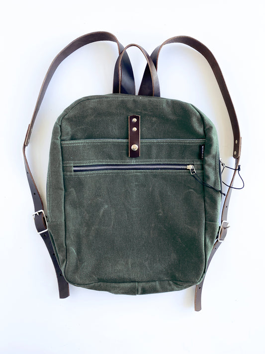 Olive, waxed cotton canvas backpack with brown leather straps.